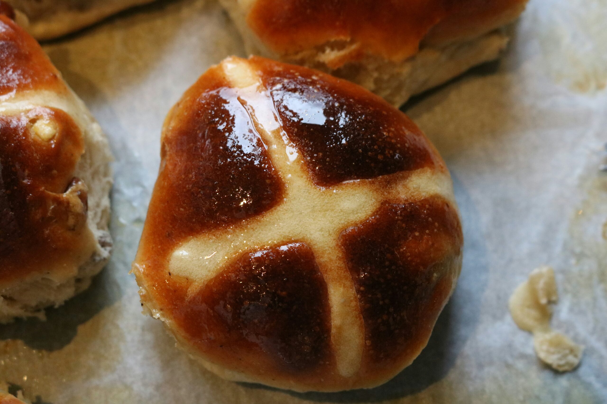 "A shiny golden bread bun with a cross on top on parchment paper "