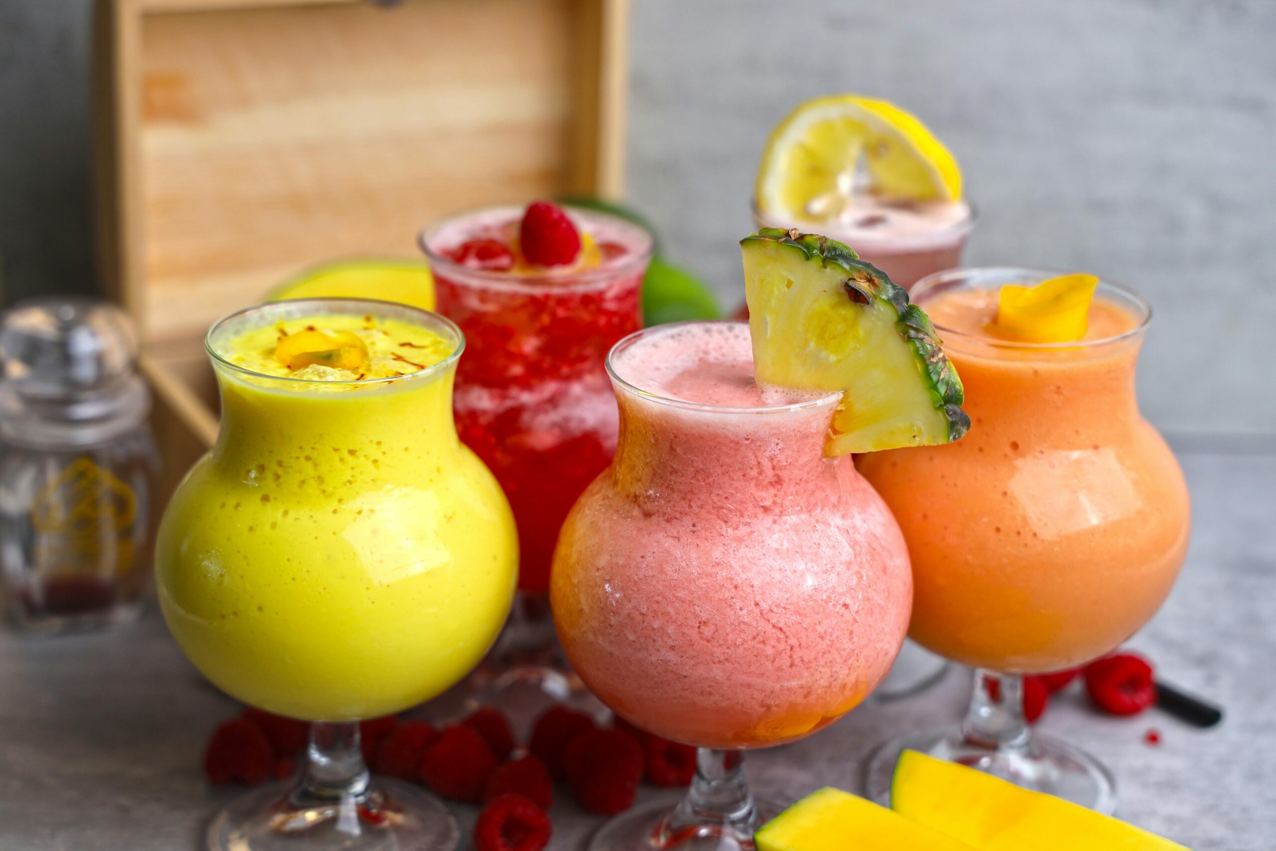"A lime green, pink, orange and red cocktail with lemon and pineapple slices on a gray background"