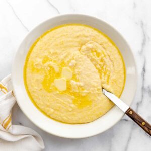 Yellow grits in a white bowl with a spoon in the bowl