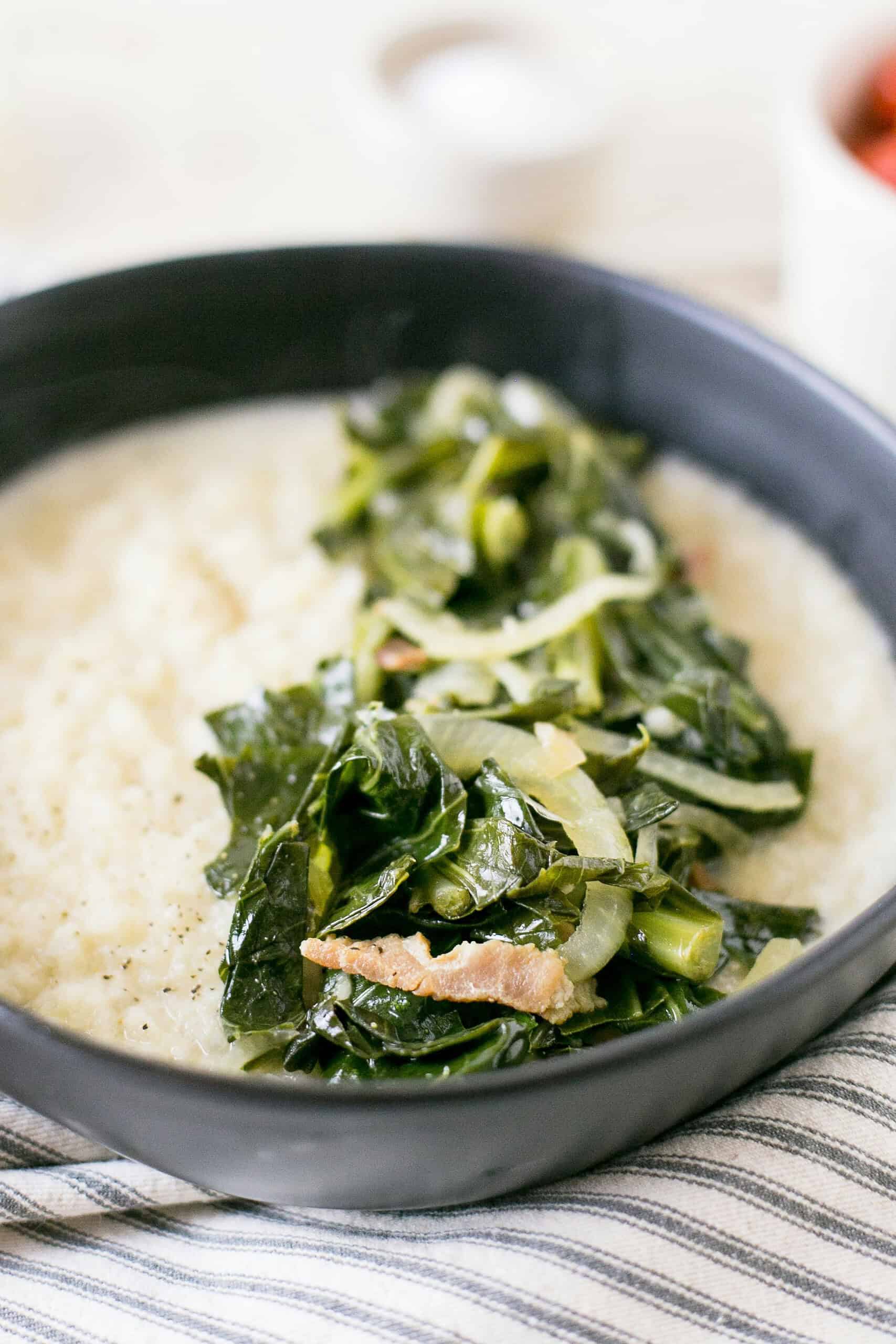 white grits in a gray bowl topped with greens on a strip towel