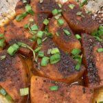 roasted sweet potatoes with spices, topped with green onions in an oven proof dish